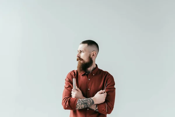 Bärtiger, gutaussehender Friseur mit Kamm und Schere in verschränkten Armen, isoliert auf weiß — Stockfoto