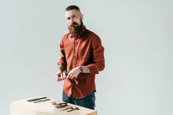 Bärtiger, gutaussehender Friseur am Tisch mit Ausrüstung, isoliert auf weißem Grund — Stockfoto