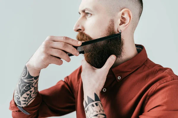 Vista lateral del hombre guapo barbudo peinando la barba aislada en blanco - foto de stock