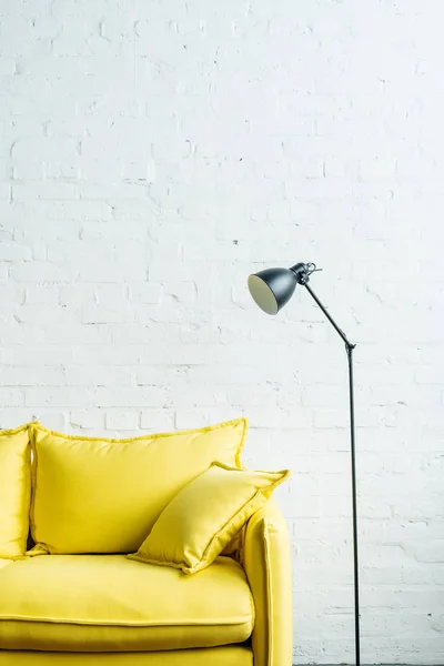 Yellow leather couch and floor lamp in front of brick wall — Stock Photo