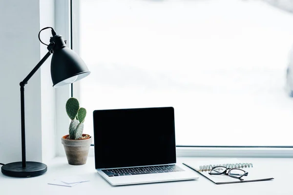 Laptop with blank screen, lamp, plant and textbook with eyeglasses — Stock Photo