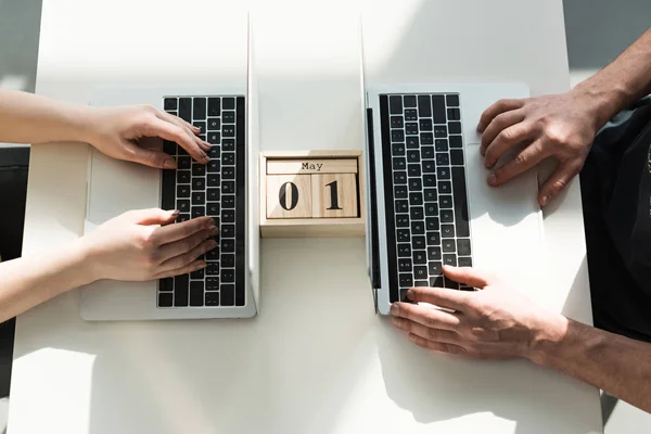 Vista dall'alto della stampa di mani maschili e femminili su computer portatili con calendario in legno tra — Foto stock