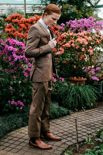 Stylish young man with red hair in suit standing glasshouse — Stock Photo