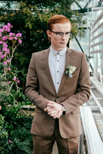 Portrait d'un homme élégant aux cheveux roux en costume et lunettes regardant loin dans la serre — Photo de stock