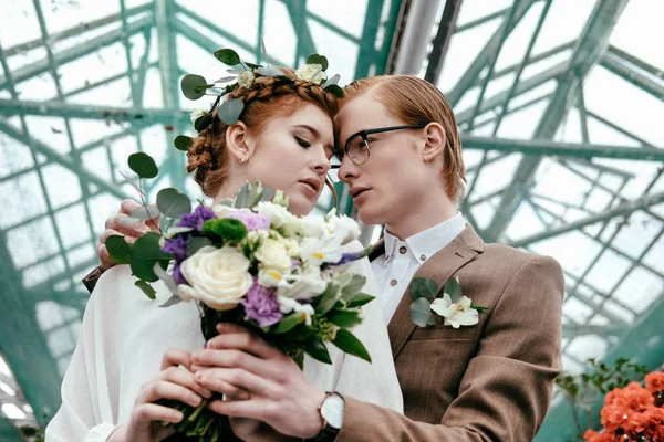 Vista de ángulo bajo de novia y novio de moda en invernadero - foto de stock