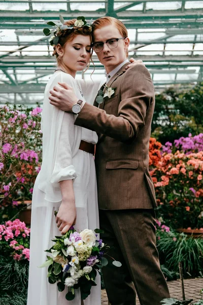 Portrait of stylish bride and groom hugging each other in greenhouse — Stock Photo
