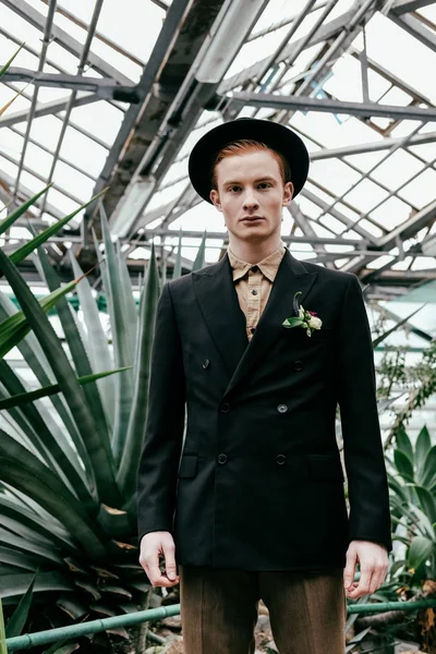 Portrait de beau homme aux cheveux roux en chapeau regardant la caméra en serre — Photo de stock