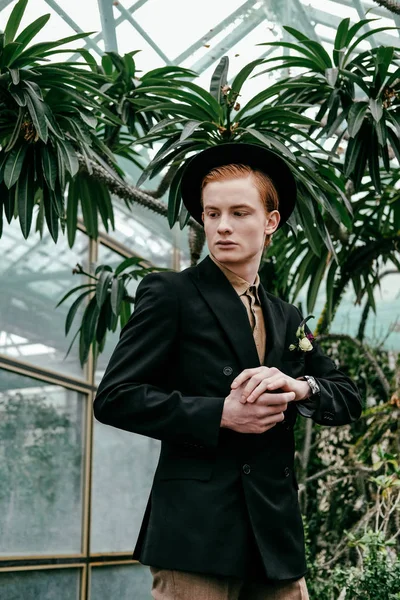 Portrait of stylish young red hair man in hat in glasshouse — Stock Photo