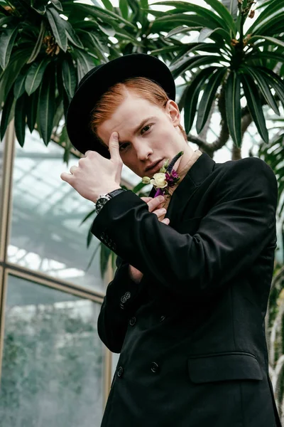 Porträt eines eleganten jungen Mannes mit rotem Haar und Hut im Glashaus — Stockfoto
