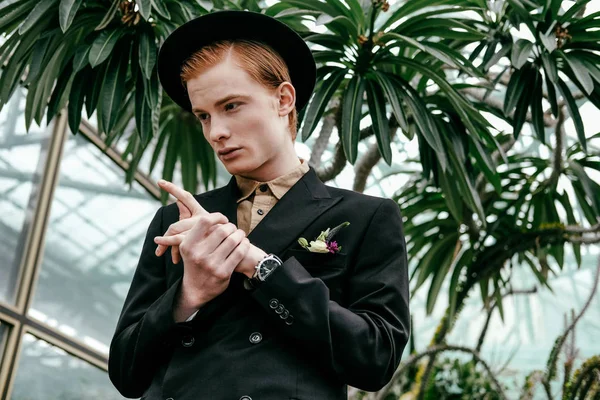Porträt eines eleganten jungen Mannes mit rotem Haar und Hut im Glashaus — Stockfoto