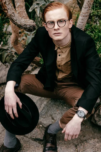 Stilvoller junger Mann mit Hut und Brille blickt in die Kamera — Stockfoto