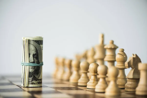 Chess pieces and rolled up cash on chess board isolated on white — Stock Photo