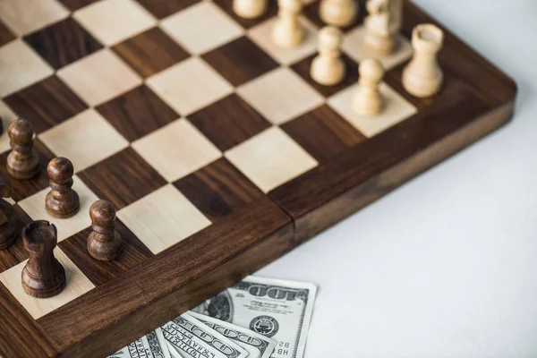 Cropped view of chess board with chess pieces and dollar banknotes on white surface — Stock Photo