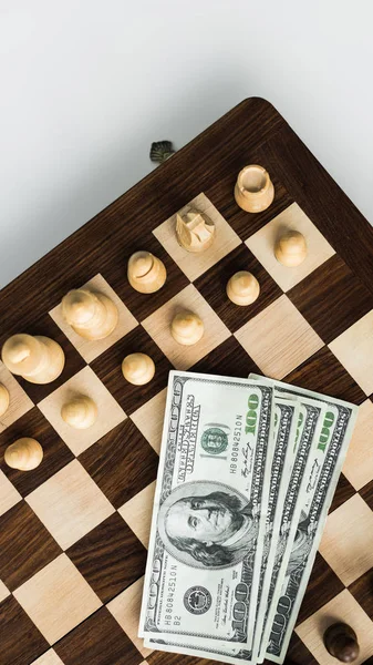 Вид зверху шахової дошки з доларовими банкнотами та шаховими фігурами на білій поверхні — стокове фото