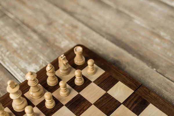 Vue recadrée de l'échiquier avec des pièces d'échecs blanches sur une surface en bois rustique — Photo de stock