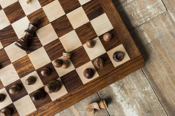 Vue du dessus de l'échiquier avec des pièces d'échecs noires éparses sur la surface en bois rusitc — Photo de stock