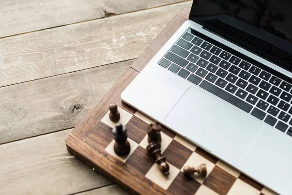 Placa de xadrez com peças de xadrez e laptop na superfície de madeira rústica — Fotografia de Stock