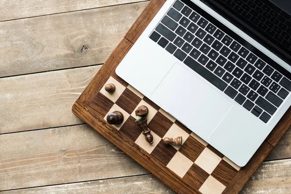 Верхний вид шахматной доски, ноутбука и шахматных фигур на деревенской деревянной поверхности — стоковое фото