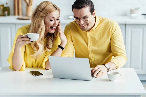 Homme et femme joyeux buvant du café et regardant l'écran d'ordinateur portable — Photo de stock