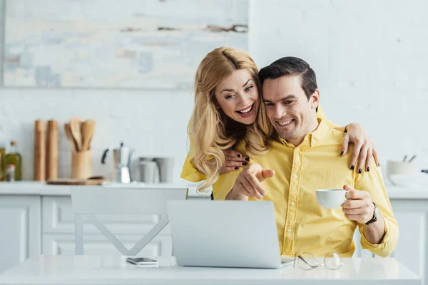 Woman hugging man who looking at laptop screen at home — Stock Photo