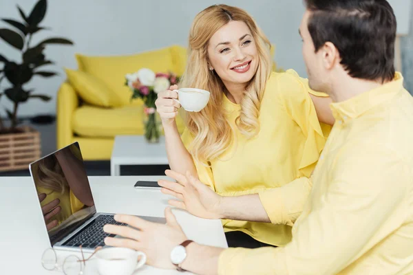 Hombre y mujer bebiendo café y trabajando por ordenador portátil en la cocina - foto de stock