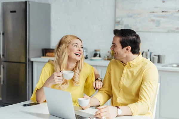 Pareja feliz bebiendo café y hablando por la mesa con el portátil - foto de stock