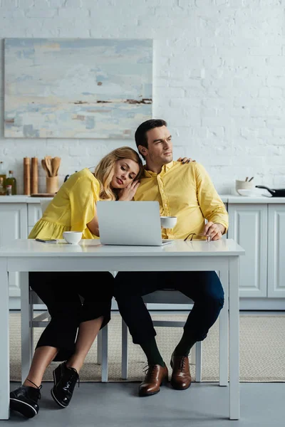 Пара пьет кофе и обнимается за столом с ноутбуком — стоковое фото