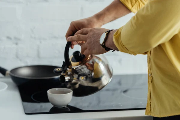 Человек наливает горячую воду в чашку на кухонный стол — стоковое фото