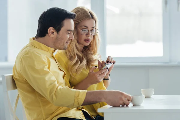 Hombre y mujer bebiendo café y mirando la pantalla del teléfono inteligente - foto de stock