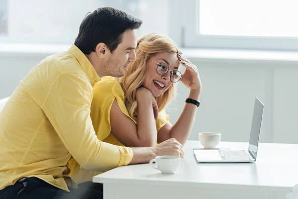 Hombre y mujer bebiendo café y mirando la pantalla del ordenador portátil - foto de stock
