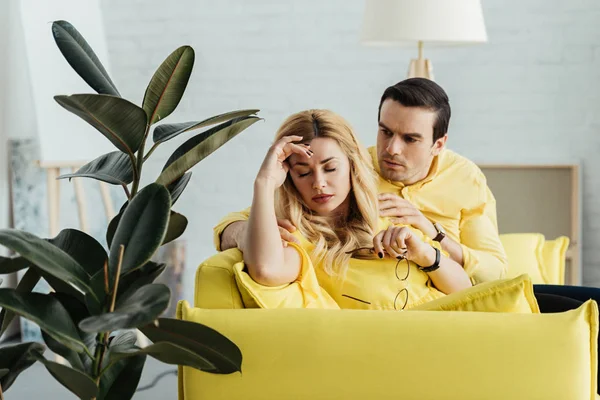 Мужчина разговаривает с расстроенной блондинкой на диване в светлой комнате — стоковое фото