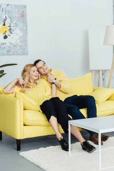 Uomo e donna romantici seduti e abbracciati sul divano giallo — Foto stock