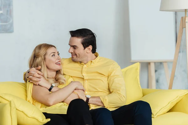Pretty couple looking at each other and sitting on yellow sofa — Stock Photo