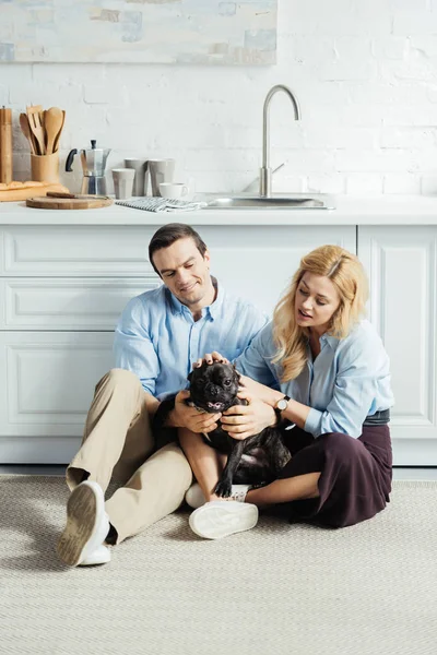 Homem feliz e mulher loira sentado no chão na cozinha com bulldog francês — Fotografia de Stock