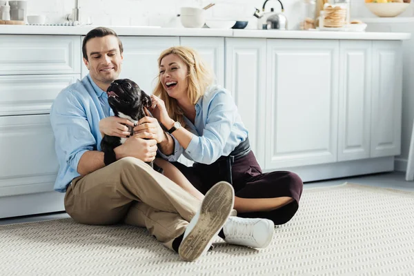 Hombre y mujer jugando con su perro en el suelo de la cocina - foto de stock