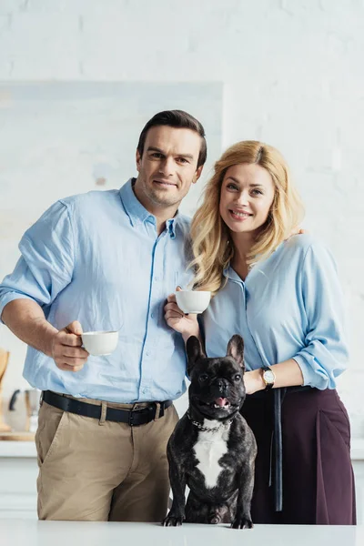 Man and woman drinking coffee by their dog on kitchen table — Stock Photo