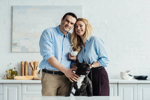 Sorridente coppia accarezzando il loro cane frenchie sul tavolo della cucina — Foto stock