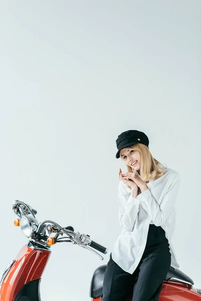 Sonriente chica rubia sentada en motocicleta vintage aislada en gris - foto de stock