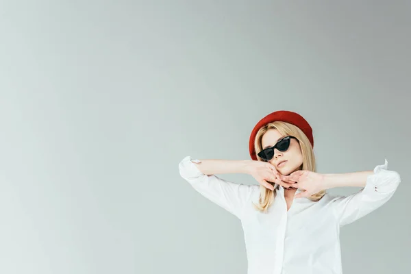 Attraktive junge Frau mit roter Baskenmütze und Sonnenbrille vereinzelt auf grau — Stockfoto