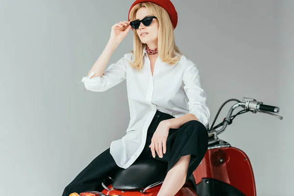Atractiva joven sentada en scooter retro aislada en gris - foto de stock
