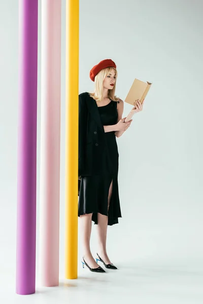 Стильна красива жінка в чорній сукні читає книгу за барвистими колонами — стокове фото