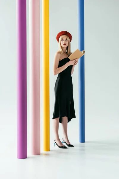 Attraktive junge Frau im schwarzen Kleid hält Buch an bunten Säulen — Stockfoto