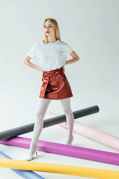 Jolie femme élégante en vêtements rouges et blancs posant parmi les rouleaux de papier colorés — Photo de stock