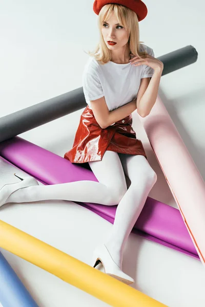 Elegant blonde girl posing among colorful paper rolls — Stock Photo