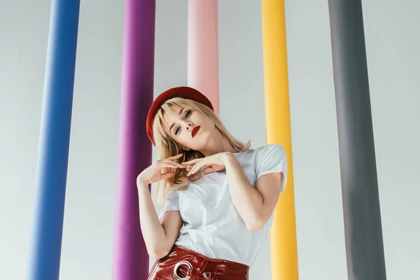 Attractive young woman in red and white clothes by colorful columns isolated on grey — Stock Photo