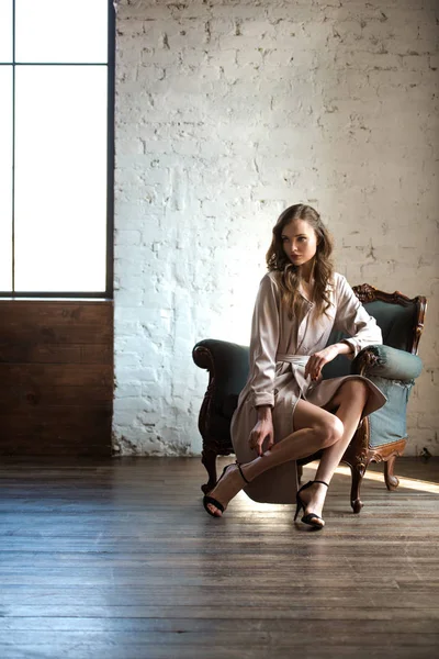 Hermosa mujer sexy en elegante gabardina posando en sillón - foto de stock