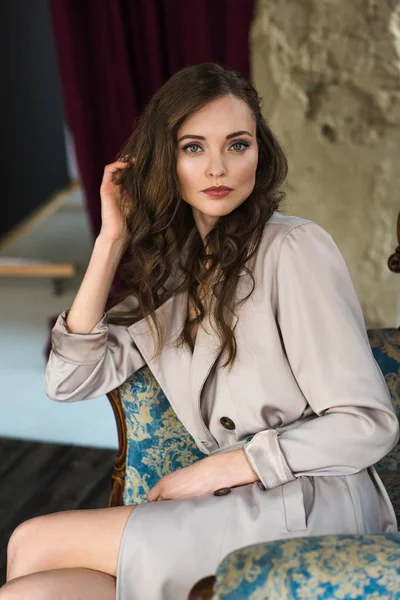 Elegant woman in fashionable trench coat sitting in armchair — Stock Photo
