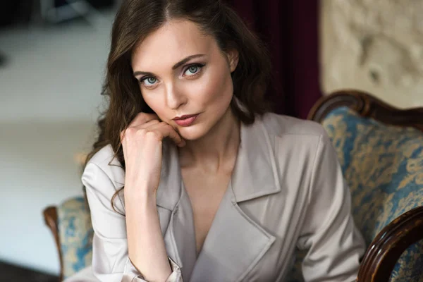 Portrait of elegant lady in beige trench coat sitting in armchair — Stock Photo