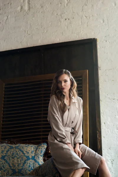 Mujer de moda en gabardina clásica posando en sillón - foto de stock