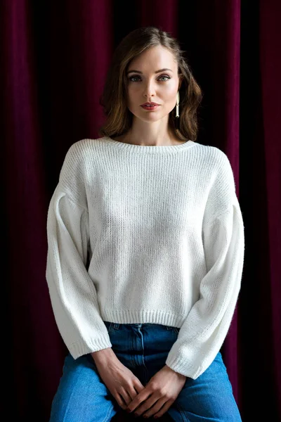 Porträt einer schönen jungen brünetten Frau in weißem Pullover und Jeans, die in die Kamera blickt — Stockfoto